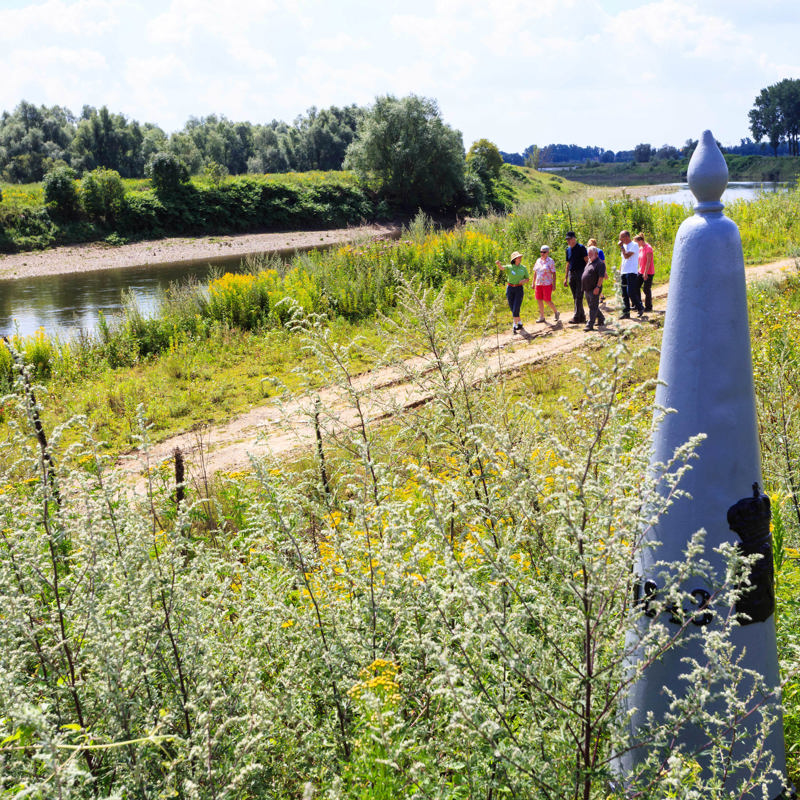 Wandelaars in het RivierPark Maasvallei met op de voorgrond een grenspaal