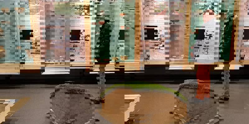 Meneer in tentoonstelling met urnen en informatiezuilen over grafstenen